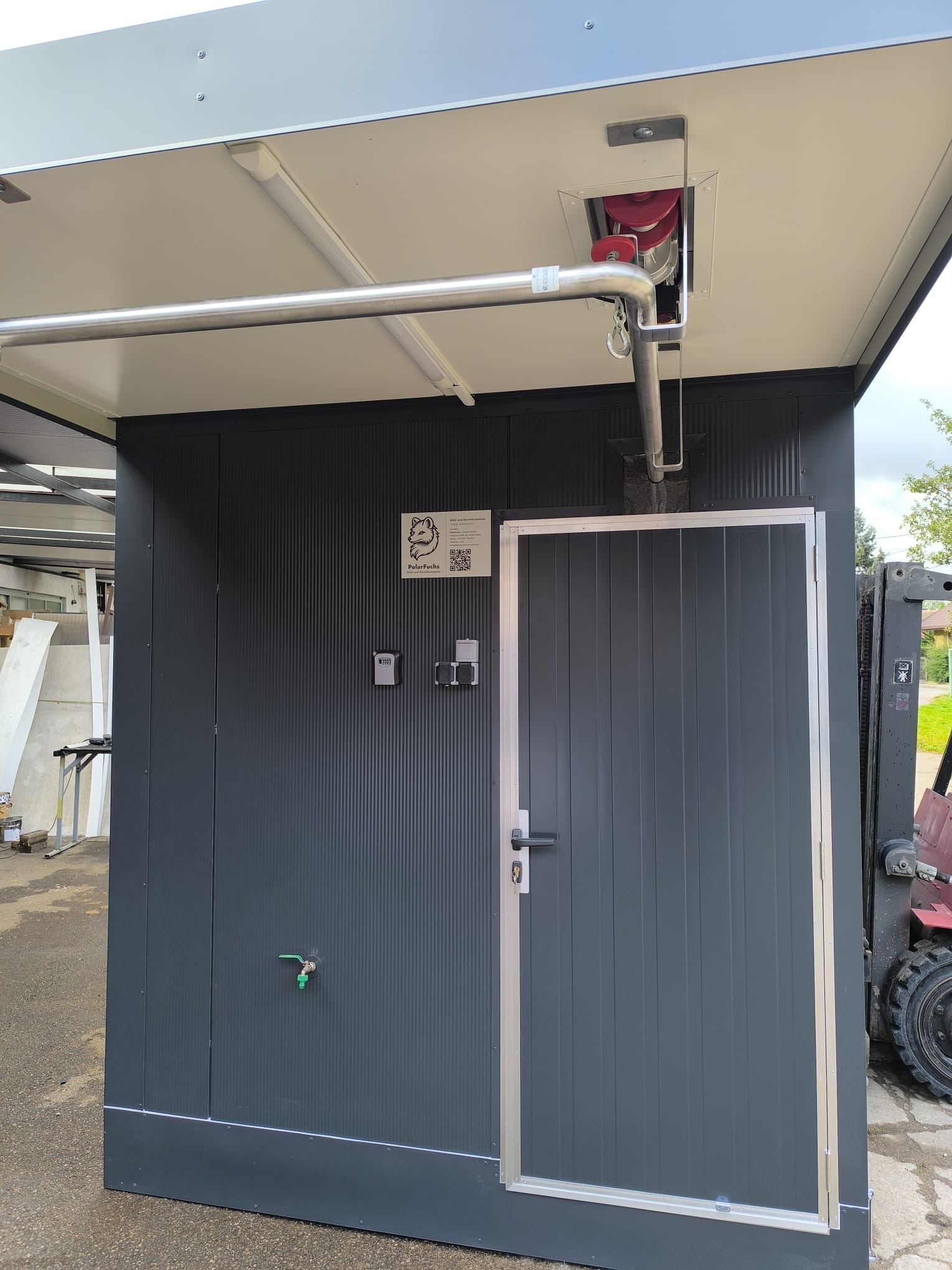 Eingangsseite der anthrazitfarbenen Kühlzelle mit Aluminium-Türrahmen, Seilwinde, Schlüsselsafe, Steckdosen und Wasserhahn